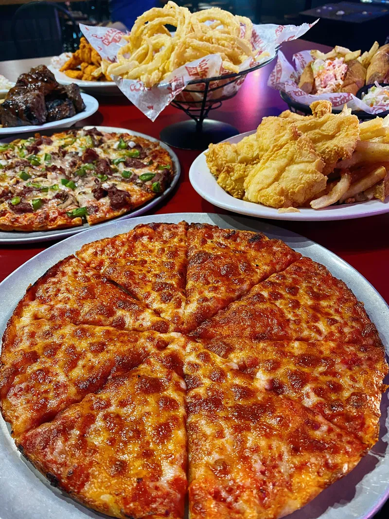 A table spread with a pizza, fried seafood, wings and onion strings